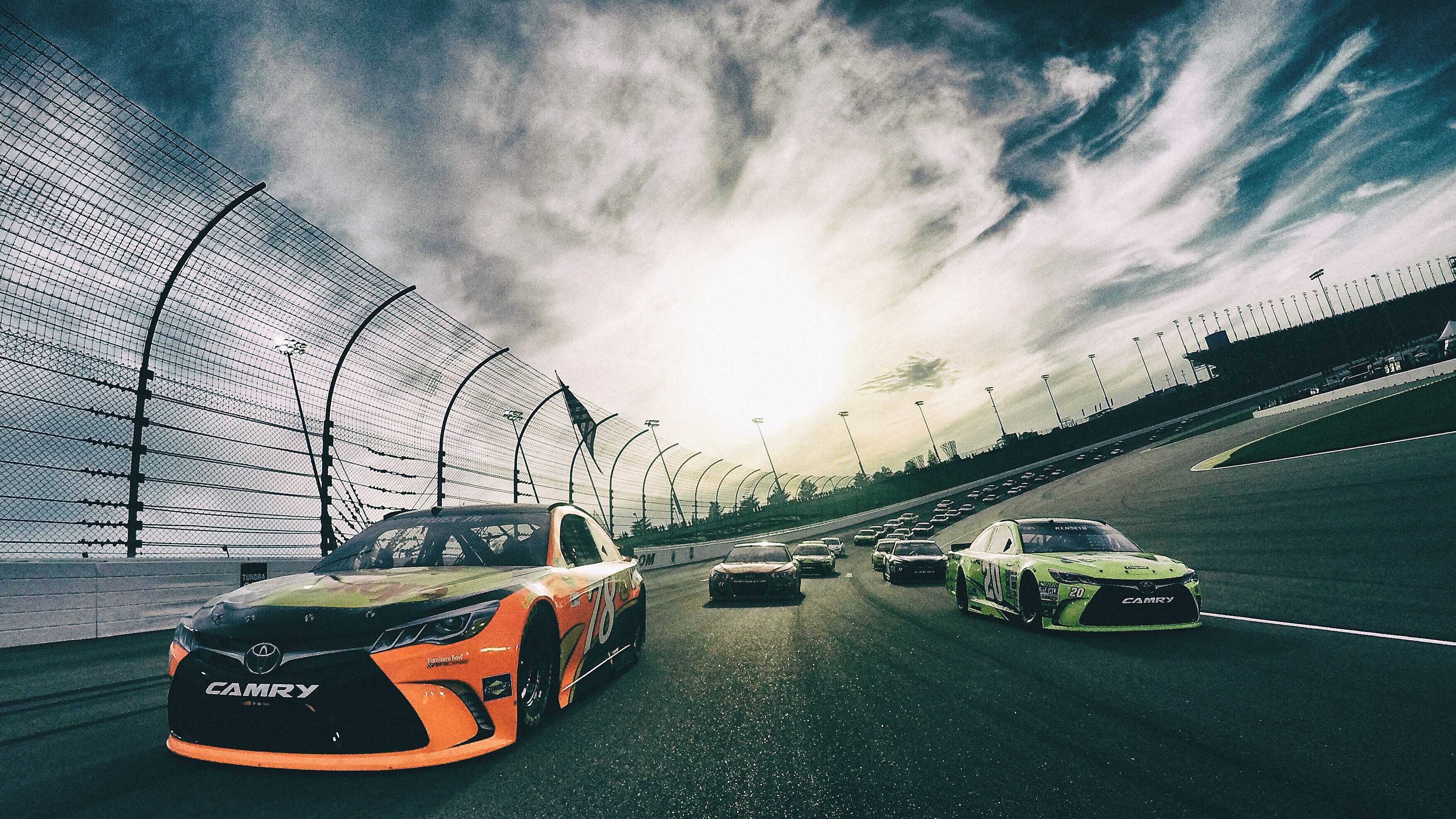 A racing track with cars, a fence, and a clear sky.