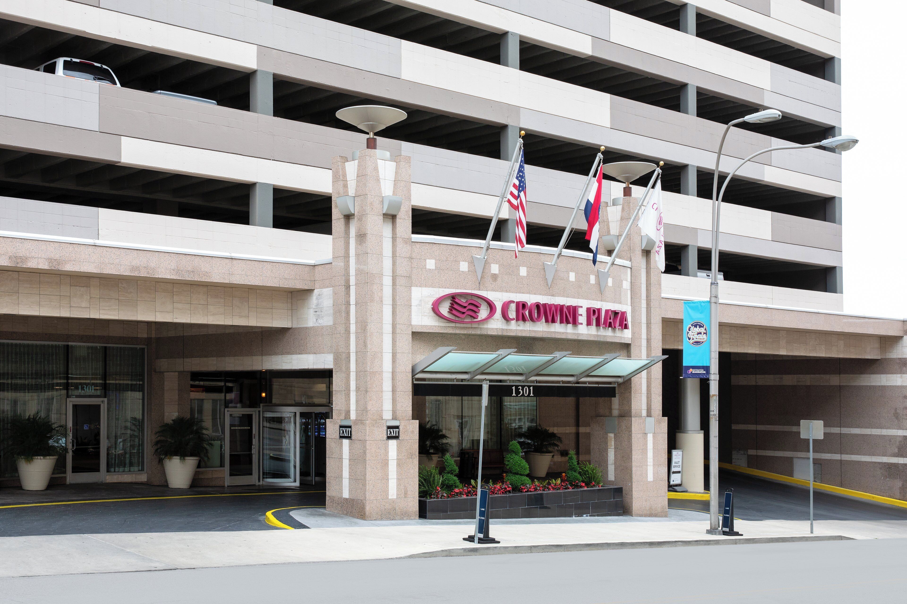 A building with a sign reading 'CROWNE PLAZA' and an American flag. There are two exit signs and a blue banner with 'Global Finals' text.