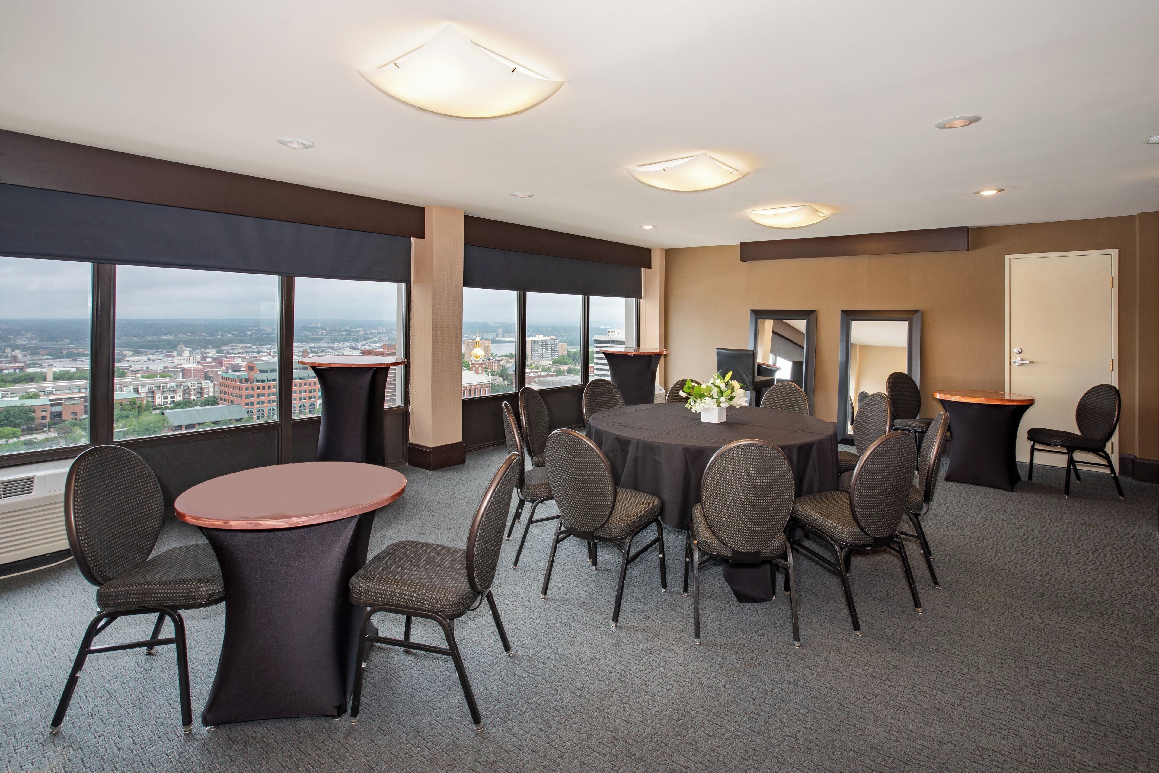 Un salón de conferencias con una mesa redonda, sillas y ventanas grandes que ofrecen vista a la ciudad.