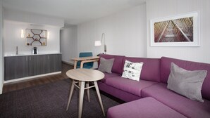 A modern living room with a purple sofa, a wooden coffee table, a kitchen area with a white countertop, and a framed picture on the wall. - Crowne Plaza Kansas City Downtown by IHG (Kansas City)