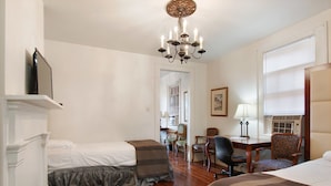 A hotel room with two beds, a desk, a chair, a chandelier, and a fireplace. - Historic Mardi Gras Inn (New Orleans)