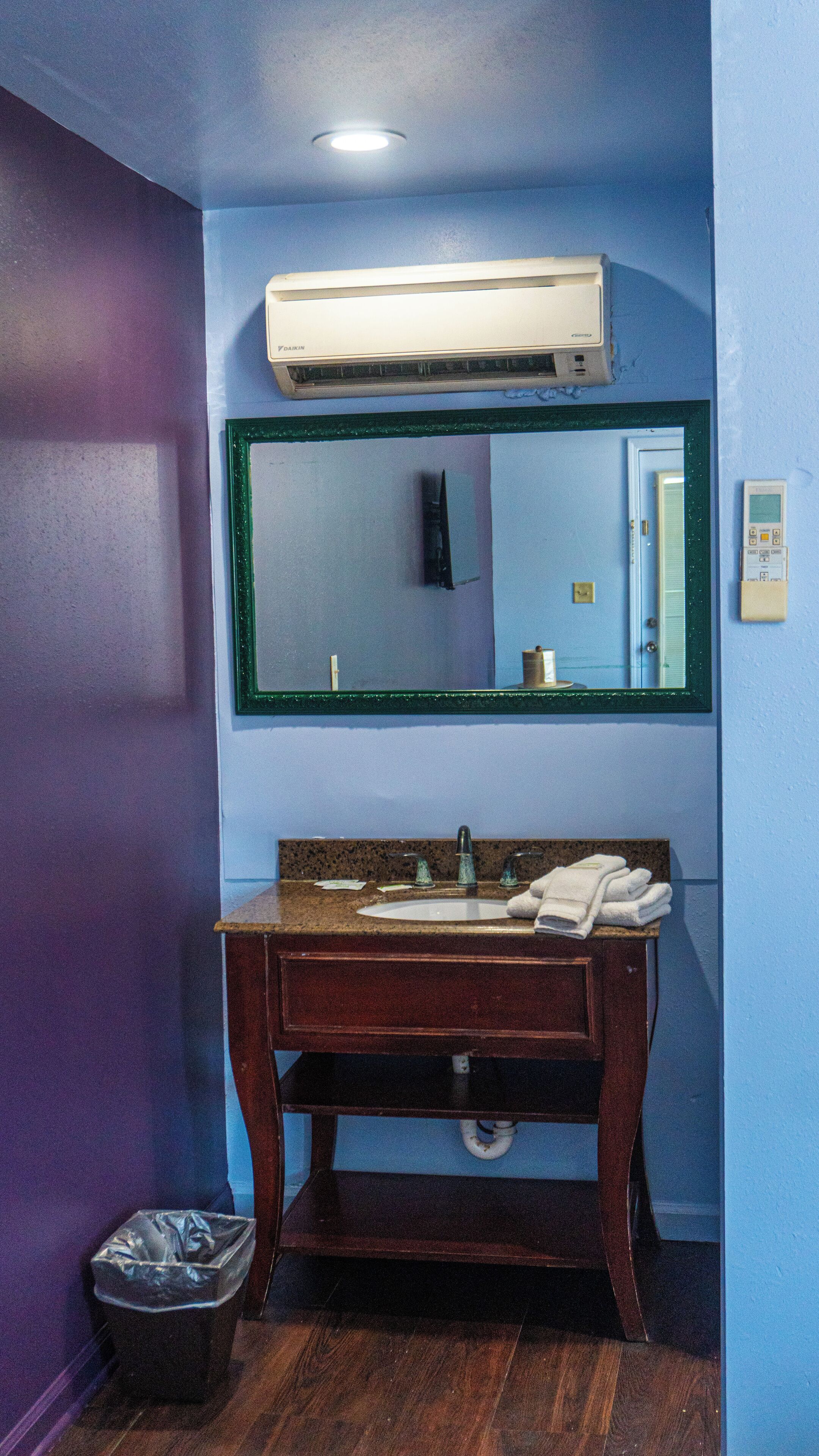 A bathroom with a wooden vanity, a mirror, a sink, a trash bin, and a wall-mounted heater.