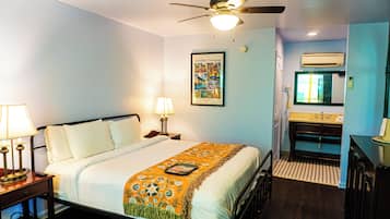 A hotel room with a bed, bedside lamps, a ceiling fan, a bathroom with a sink and mirror, and an air conditioning unit.