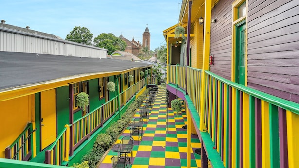 A narrow outdoor corridor with a checkered floor, green railings, and yellow and purple walls. - Historic Mardi Gras Inn (New Orleans)