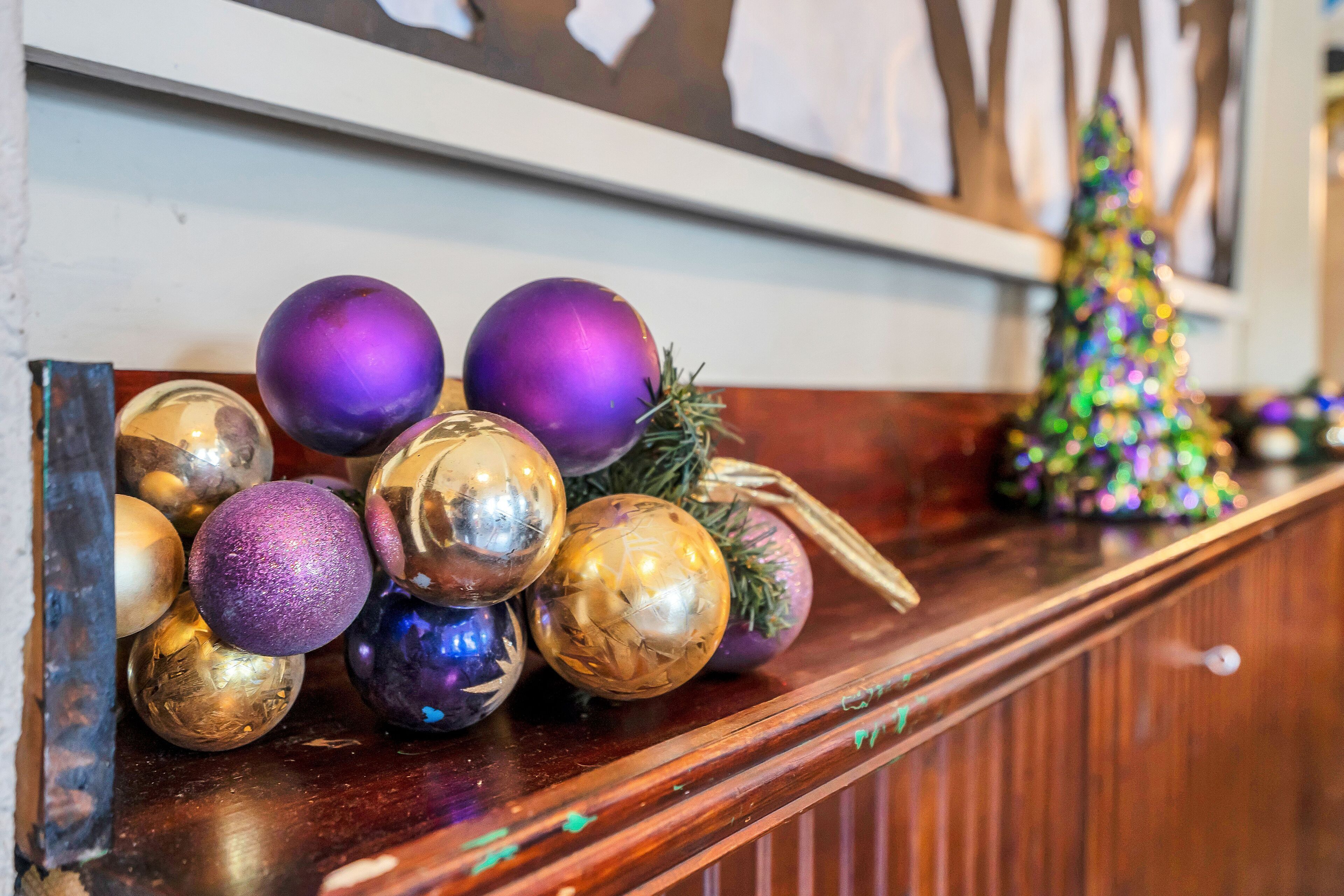 Una repisa de madera adornada con diversos objetos decorativos, incluyendo esferas moradas y doradas, y un pequeño árbol de Navidad.