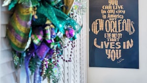 A wall with a decorative wreath and a framed quote about New Orleans. - Historic Mardi Gras Inn (New Orleans)
