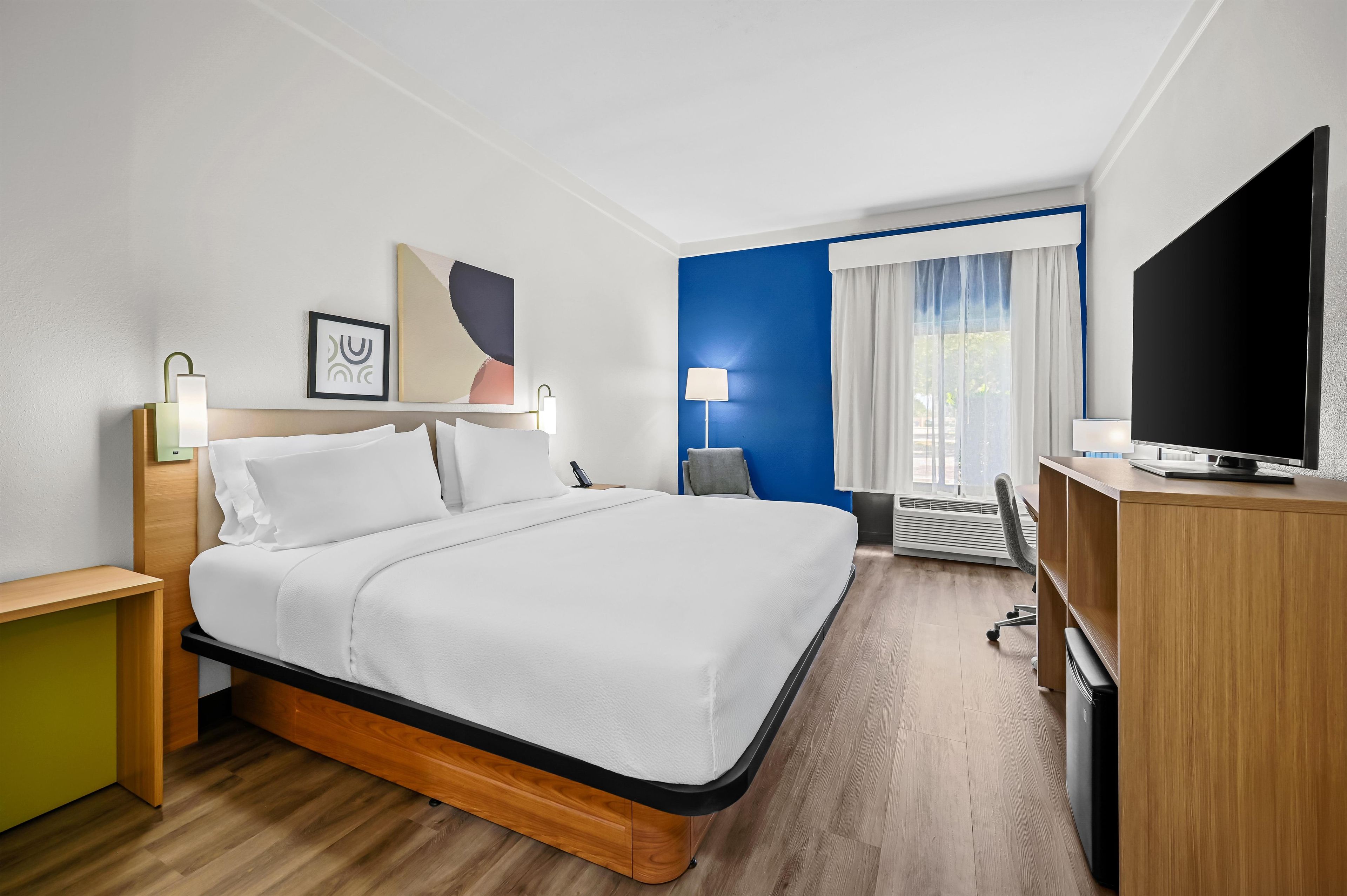 Habitación de hotel con cama, escritorio, televisor y ventana con cortinas.