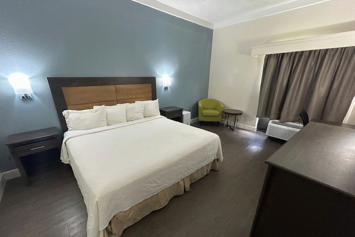 A hotel room with a large bed, bedside tables, a chair, a desk, and a window with curtains.
