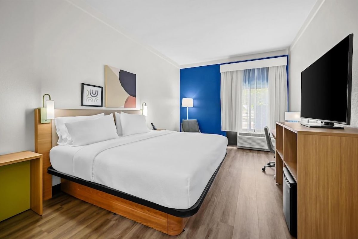A hotel room with a bed, desk, TV, and a window with curtains.