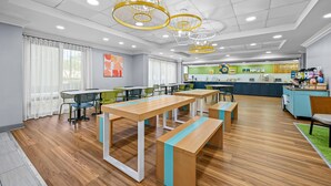 A modern dining area with wooden tables and benches, a kitchen in the background, and a ceiling with recessed lighting and decorative fixtures.