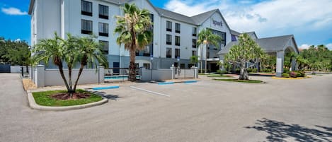 A modern hotel with a parking lot, palm trees, and a clear blue sky.