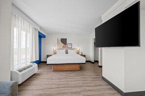 A modern hotel room with a bed, bedside tables, a flat-screen TV, and a large window with curtains.