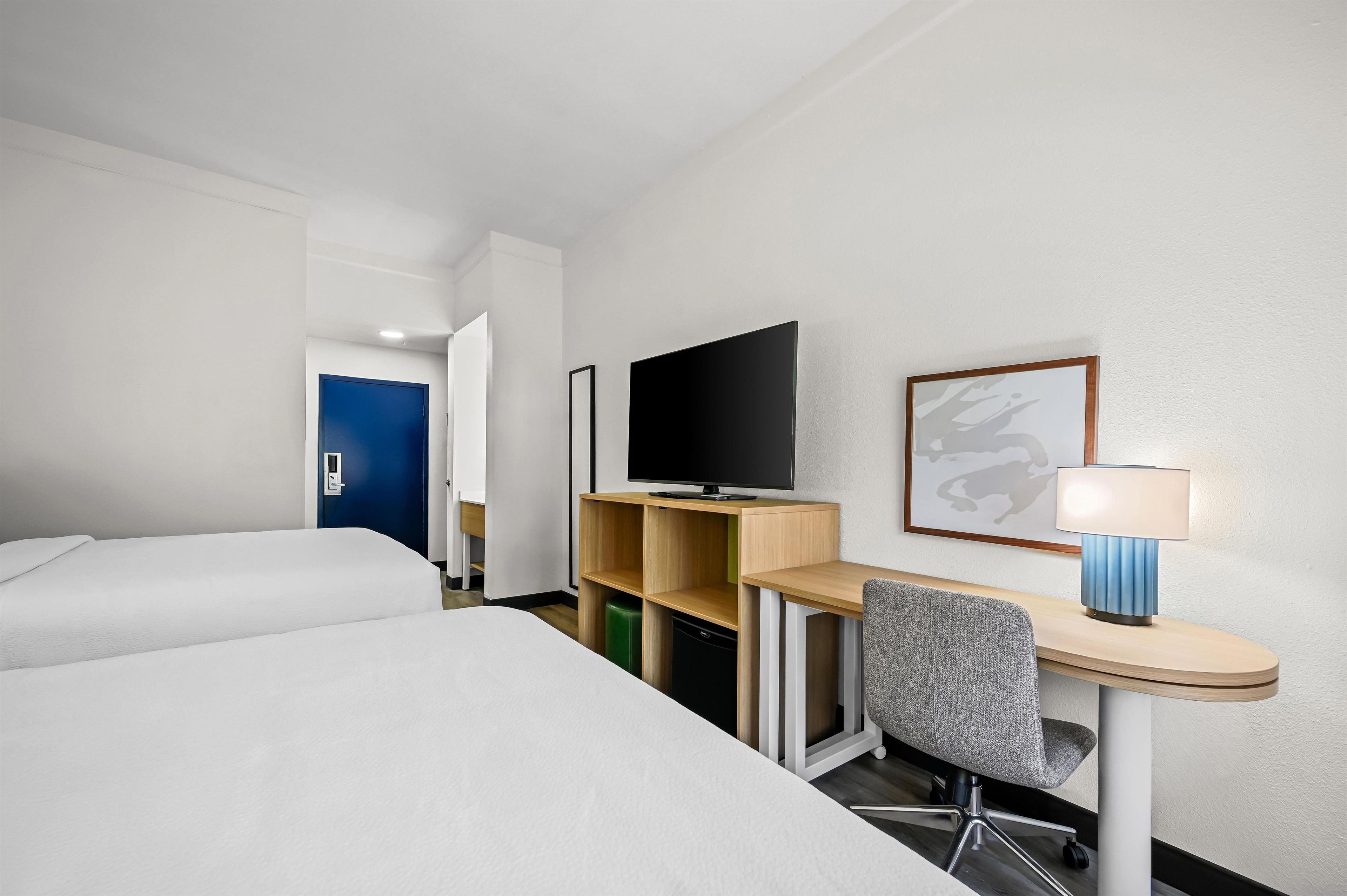 Una habitación de hotel con cama, escritorio, silla, televisor y lámpara.