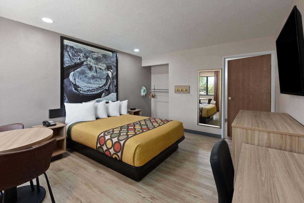 A hotel room with a bed, a desk, a chair, a mirror, and a painting on the wall.