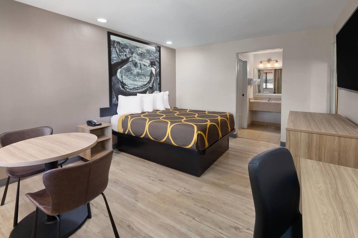 A modern hotel room with a large bed, a desk, a chair, and a dining table.