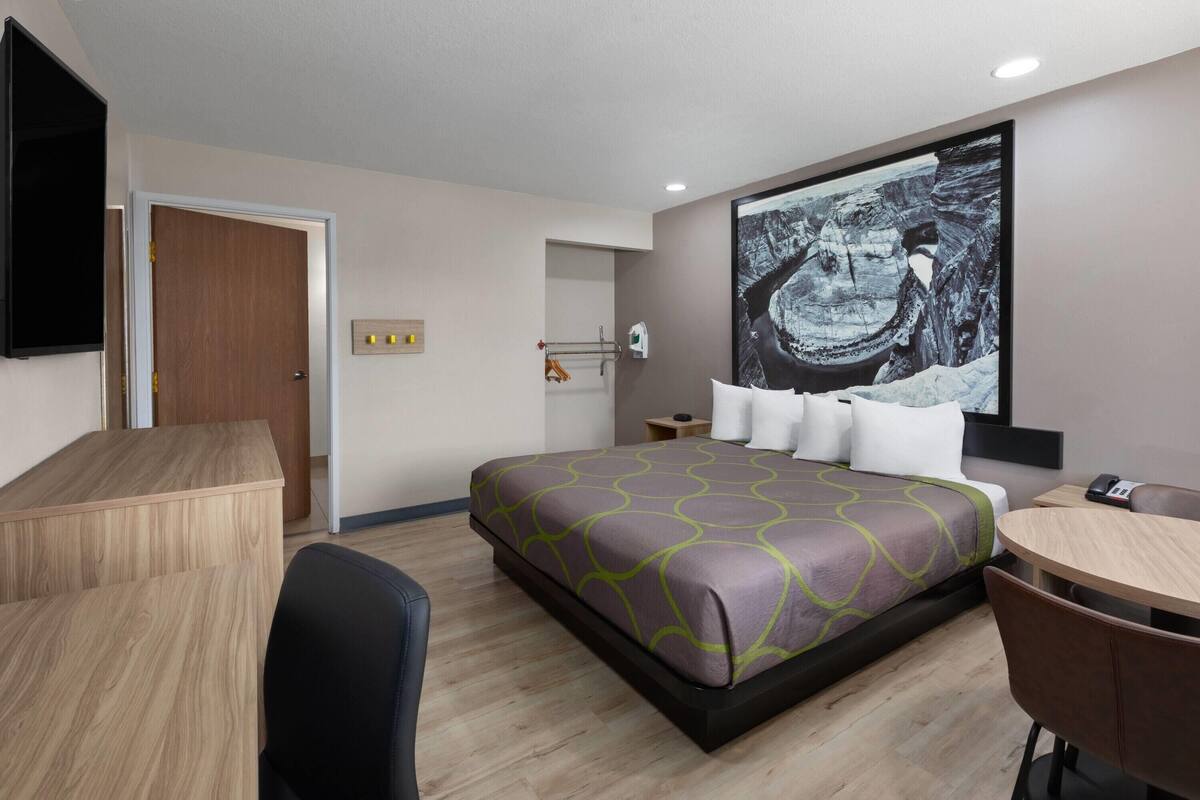 A hotel room with a bed, a desk, a chair, a TV, and a large painting on the wall.