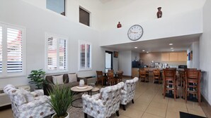 Amplia sala de estar con sofá, sillones y mesa de comedor. Se observa una cocina al fondo con armarios de madera y un reloj en la pared.