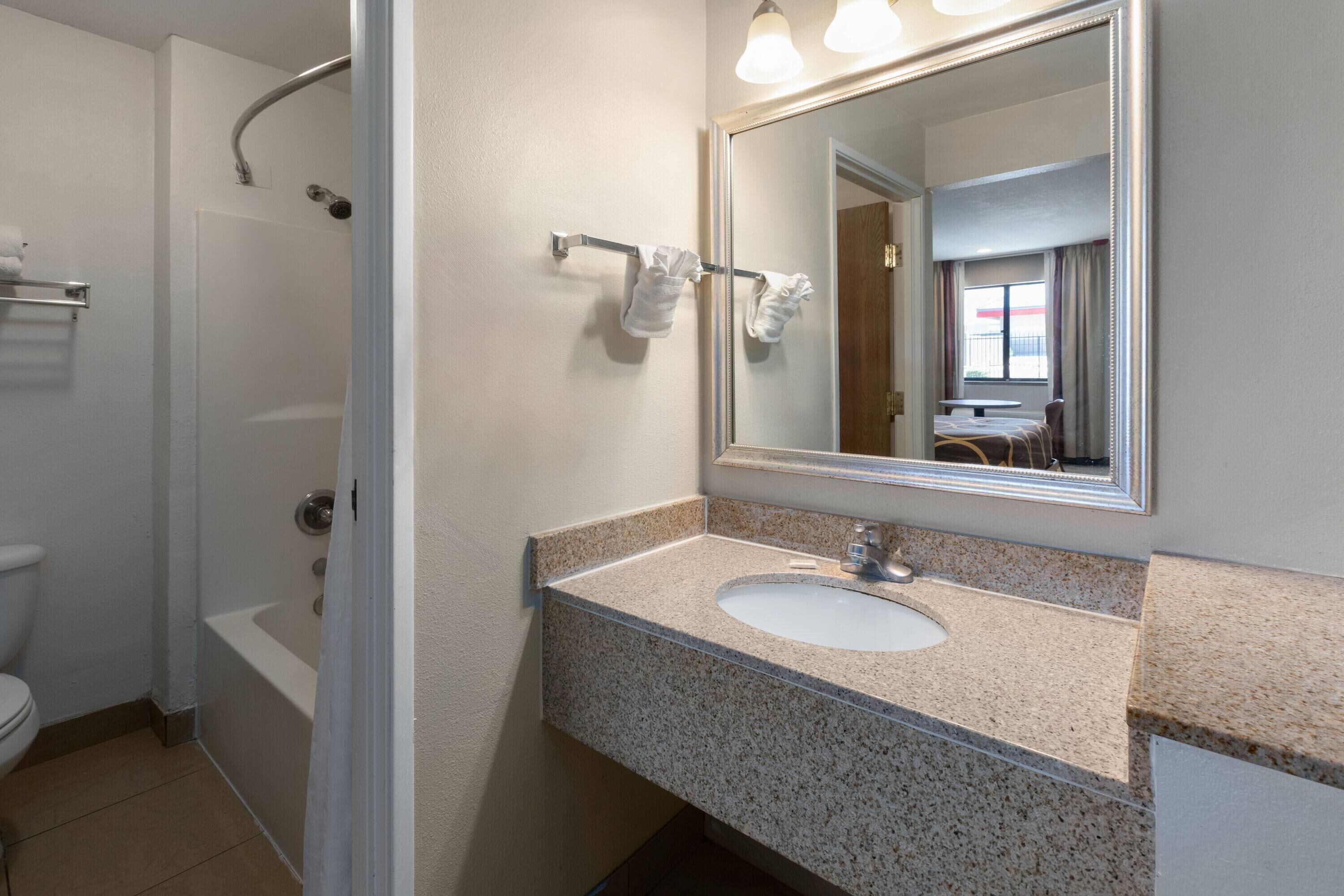 A bathroom with a sink, mirror, towel rack, shower, and toilet.
