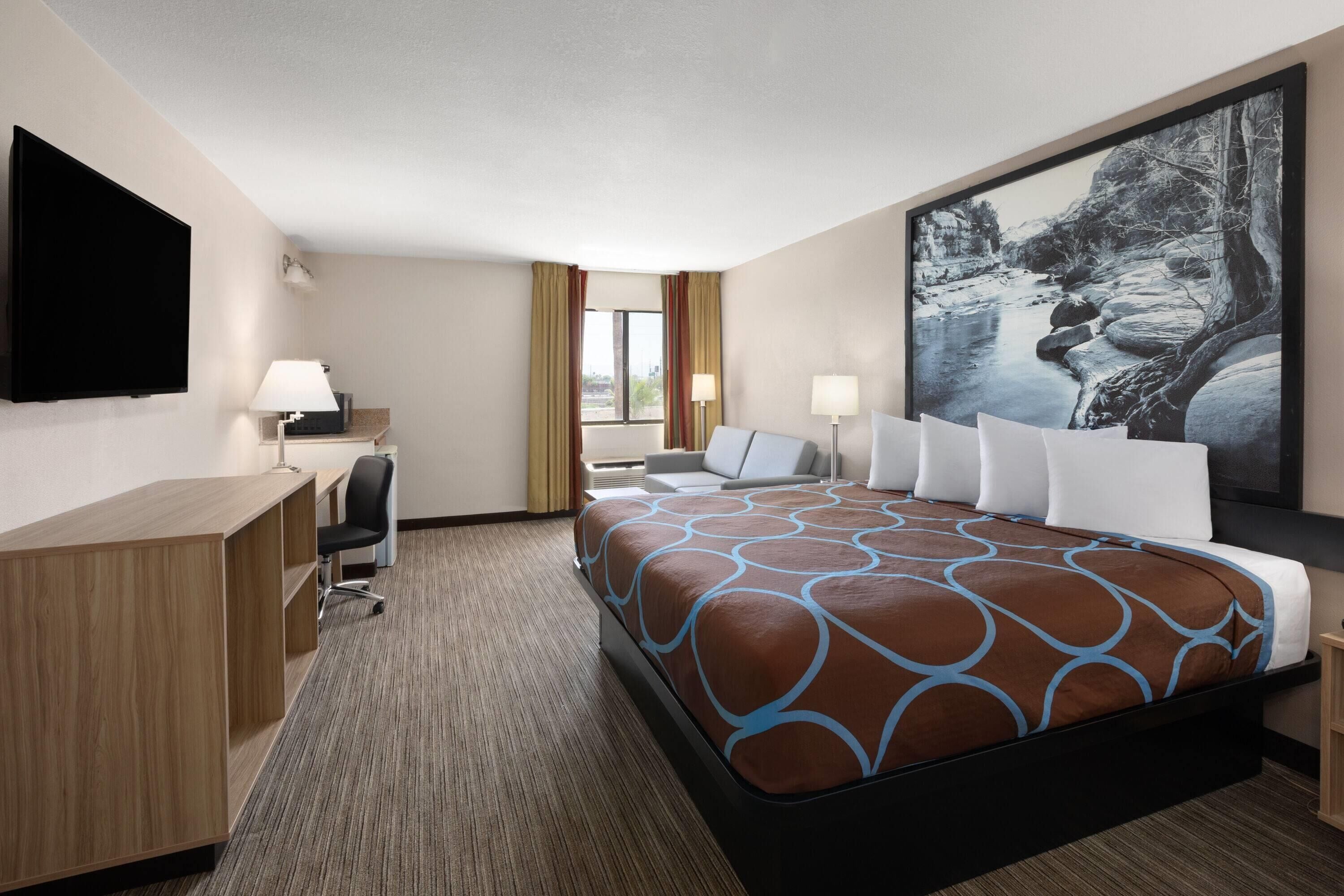 A hotel room with a large bed, a desk, a chair, a TV, and a painting on the wall.