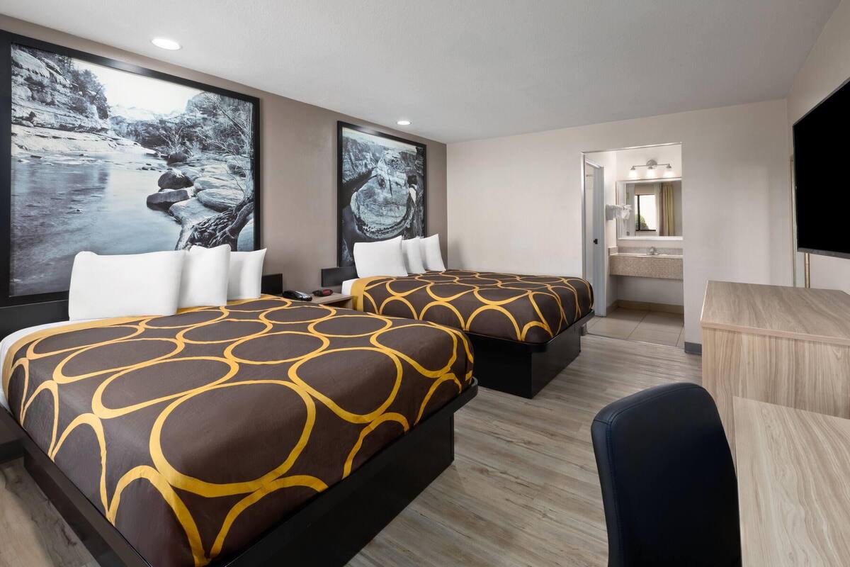 A hotel room with two beds, a desk, and a large window.