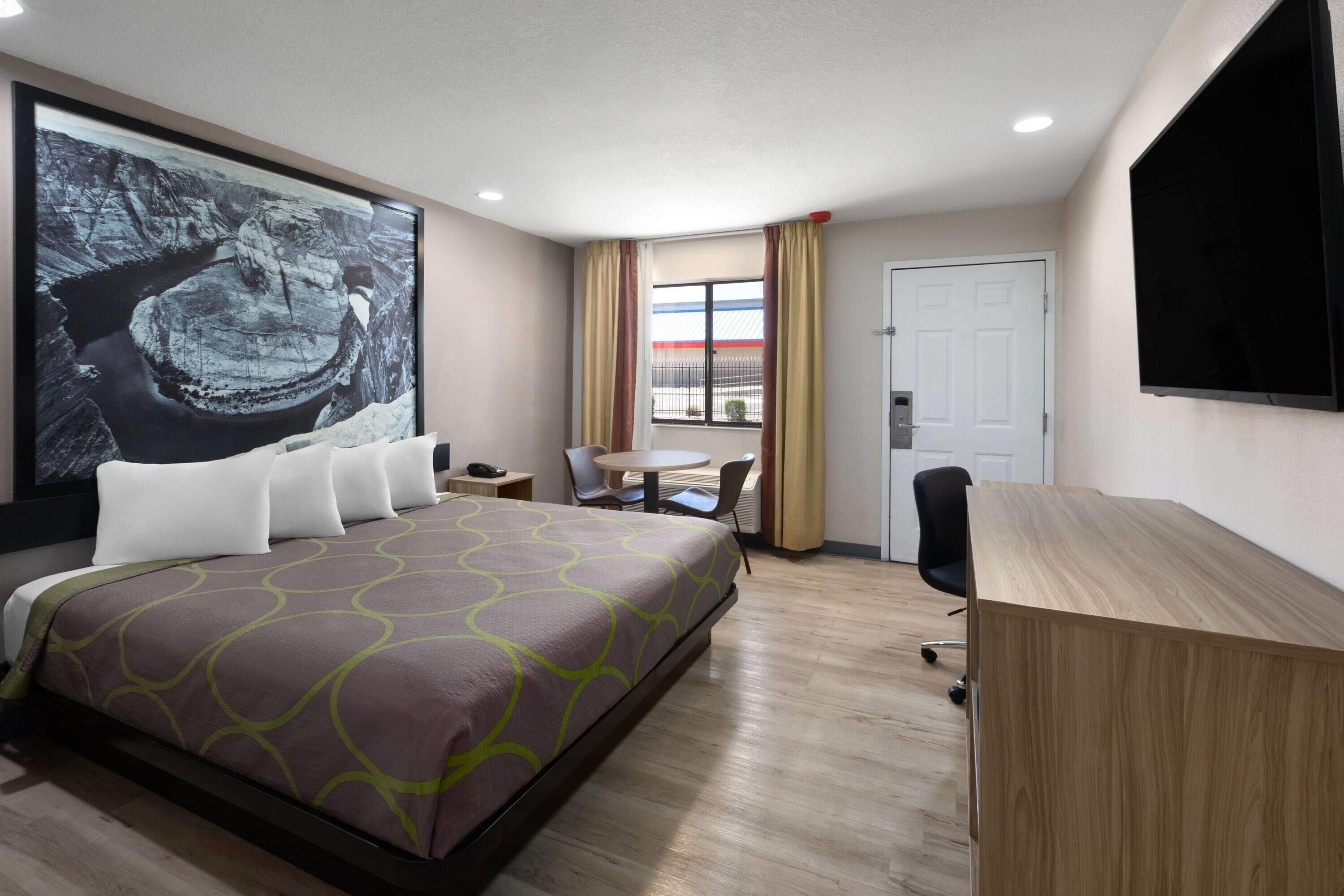 Habitación de hotel con una cama grande, un escritorio, una silla, una mesita y un ventanal con cortinas.