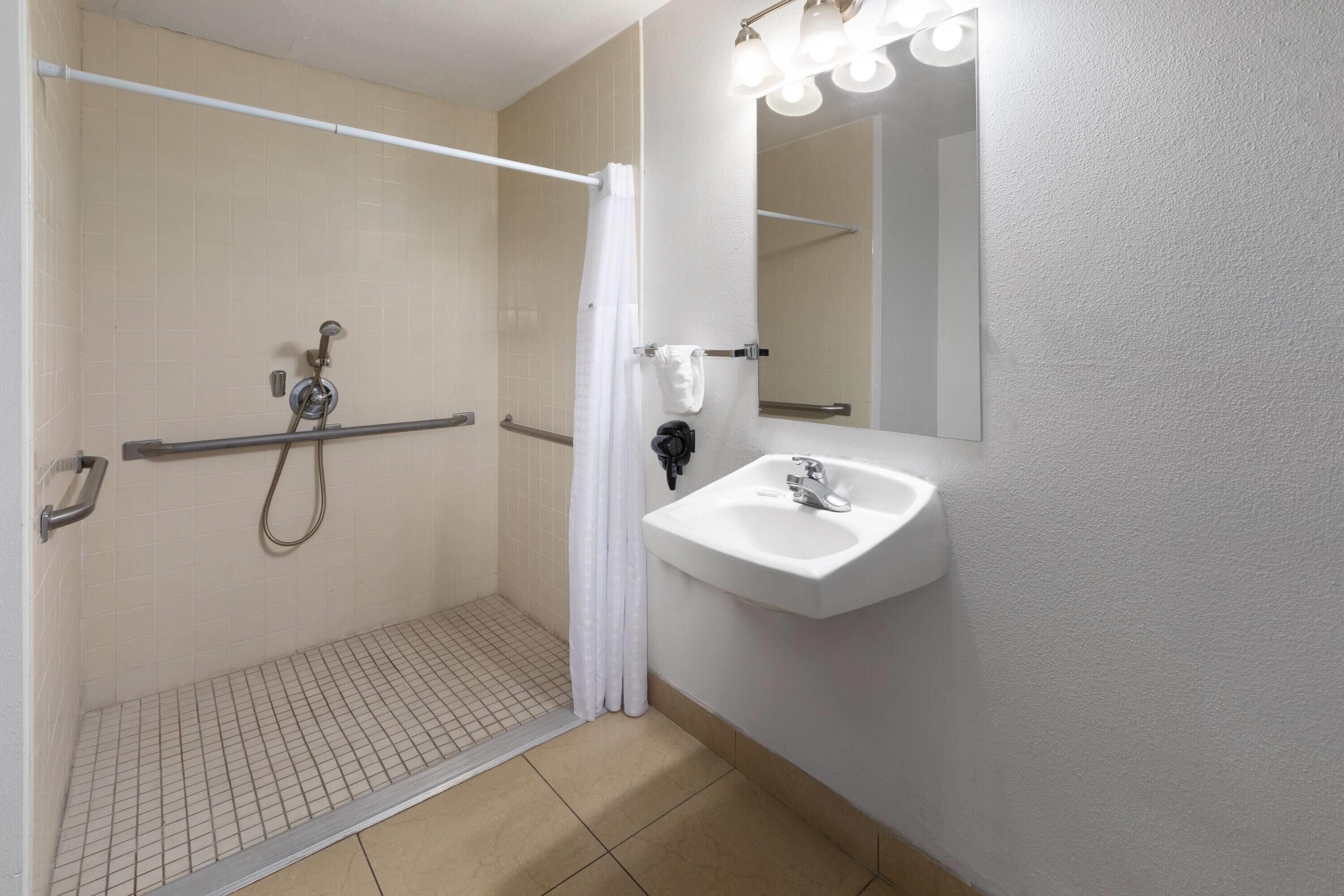 Un baño con cabina de ducha, barra de apoyo y lavabo con espejo.