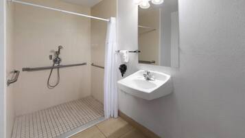 Un baño con cabina de ducha, barra de apoyo y lavabo con espejo.