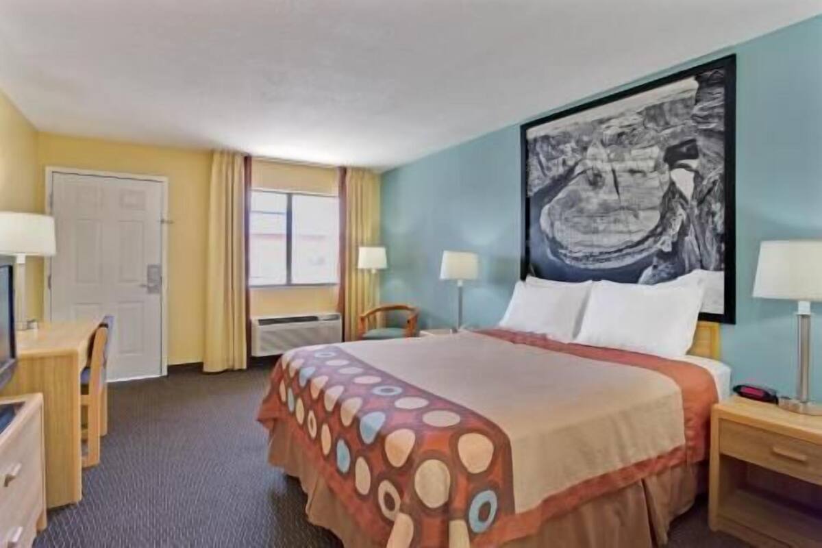 A hotel room with a bed, two bedside tables, a desk, a chair, a window, and a wall-mounted painting.