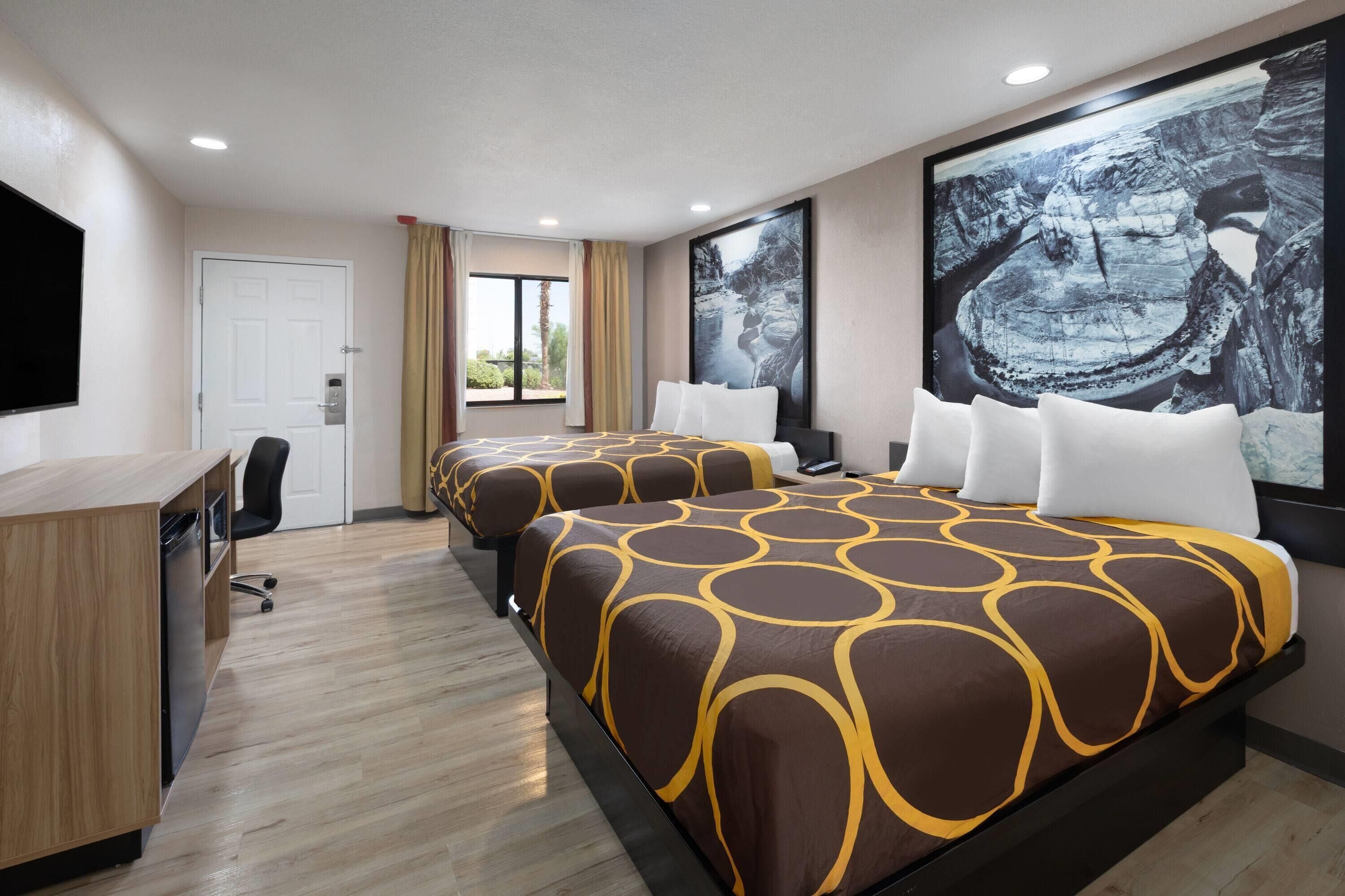A hotel room with two beds, a desk, and a large window.