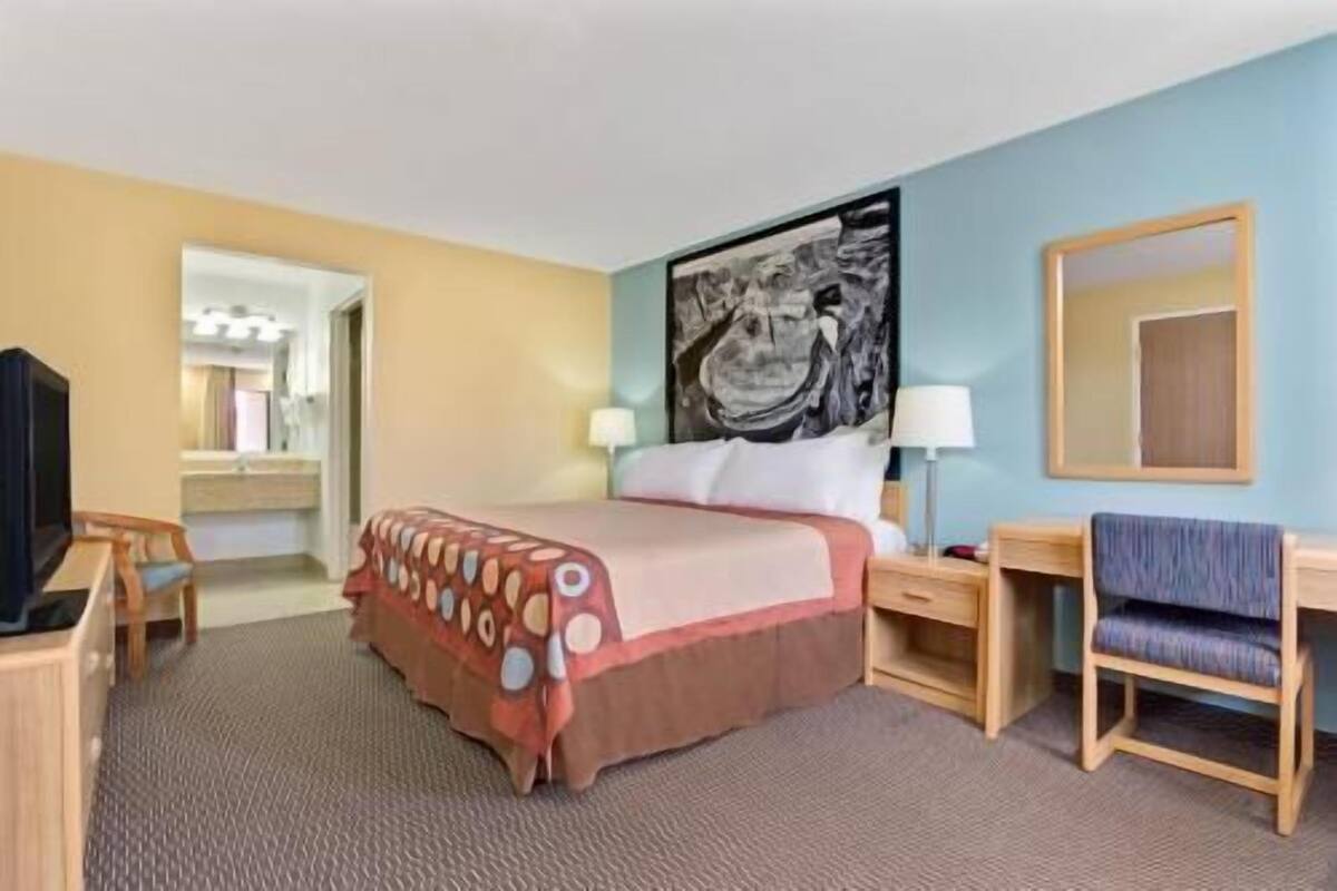 A hotel room with a bed, a desk, a chair, a TV, and a painting on the wall.