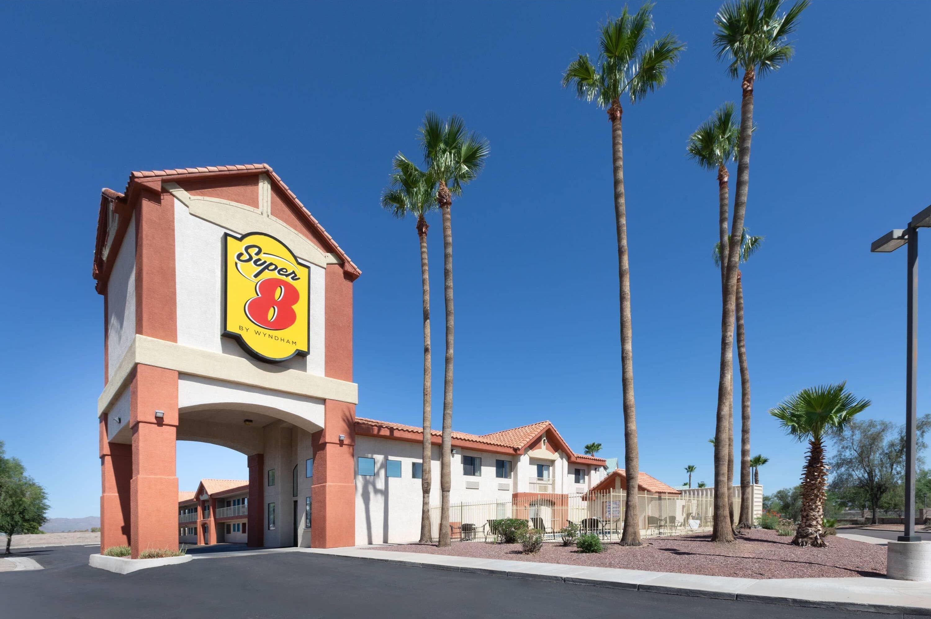 A hotel entrance with a prominent sign, palm trees, and a clear blue sky.