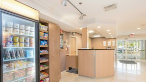 A clean, well-lit lobby with a refrigerated display case filled with snacks and beverages, a reception desk, and a glass door leading outside. - Fairfield Inn & Suites By Marriott - Brunswick (Brunswick)