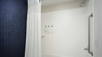 Um banheiro com uma banheira branca, um chuveiro com chuveiro manual e três frascos de shampoo na parede.
