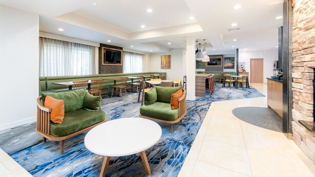 A modern hotel lobby with a seating area, a bar, and a kitchen in the background. - Fairfield Inn & Suites By Marriott - Brunswick (Brunswick)