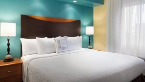 Ein Hotelzimmer mit einem großen Bett, zwei Nachttischen mit Lampen, Wänden in Türkis und Gelb sowie einem Fenster mit durchsichtigen Vorhängen.