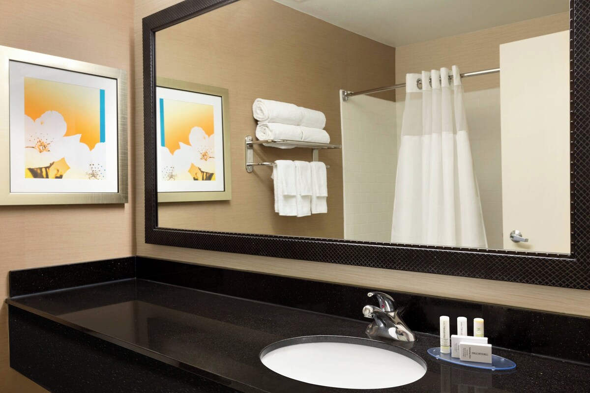 A hotel bathroom with a large mirror, a black countertop, a white sink, and a towel rack with folded towels.