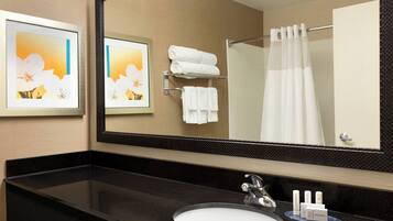 A hotel bathroom with a large mirror, a black countertop, a white sink, and a towel rack with folded towels.