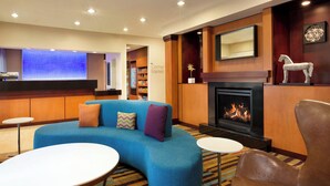 Eine moderne Hotelhalle mit einem blauen Sofa, einem Kamin, einem kleinen Tisch und einer Rezeption mit blauer Wand und dem Schild "The Corner Market".