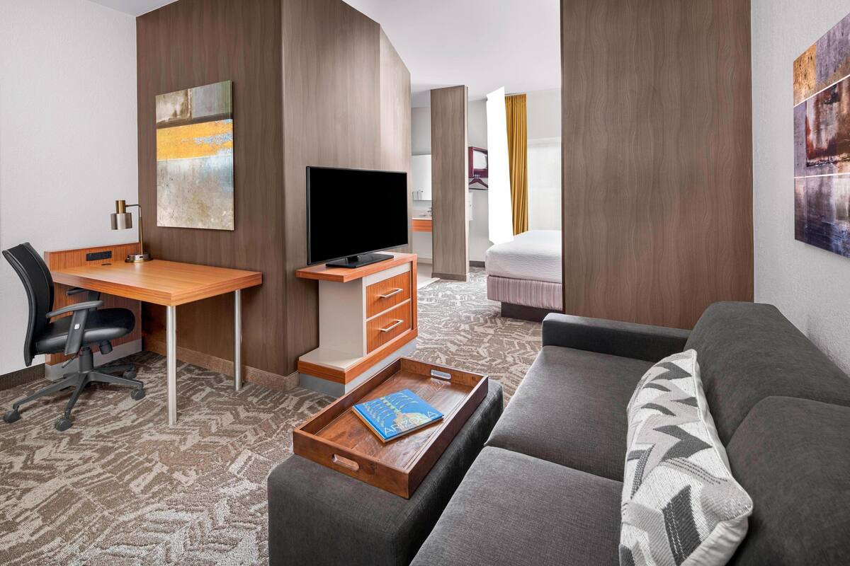 Habitación de hotel con escritorio de madera, televisor de pantalla plana, sofá y una mesita con un libro.