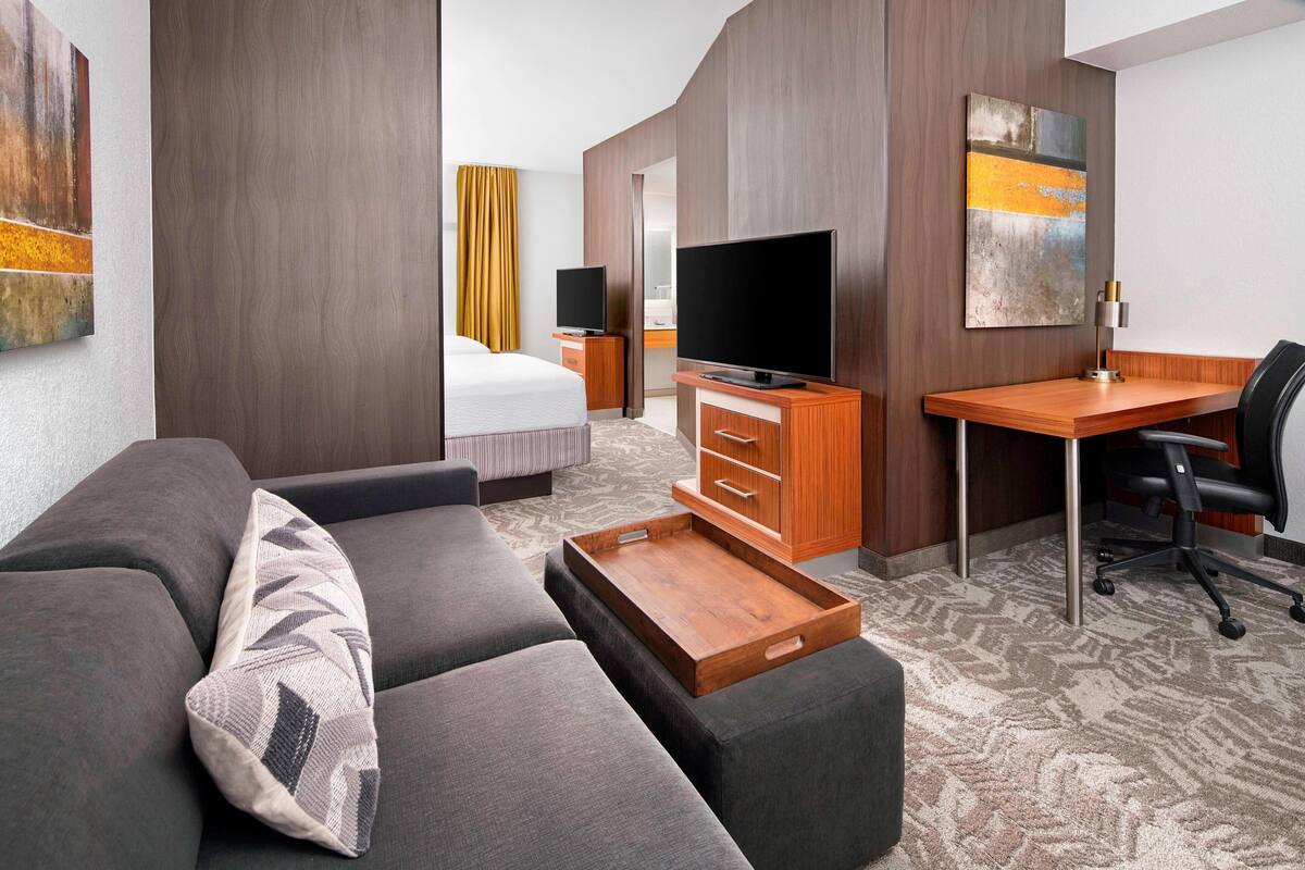 Una habitación de hotel moderna con un sofá, un escritorio de madera, un televisor y obras de arte en las paredes.