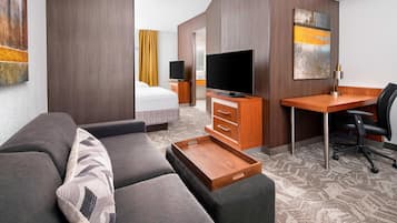 A modern hotel room with a sofa, a wooden desk, a television, and artwork on the walls.