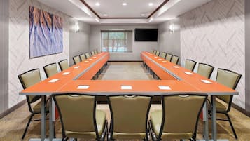 Un salón de conferencias con una larga mesa y sillas, un cuadro grande en la pared y una ventana con vistas.