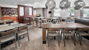 A modern restaurant with wooden tables and chairs, a counter with a display, and large windows.