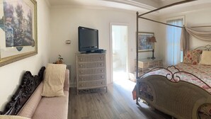 A bedroom with a four-poster bed, a dresser, a television, and a painting on the wall.