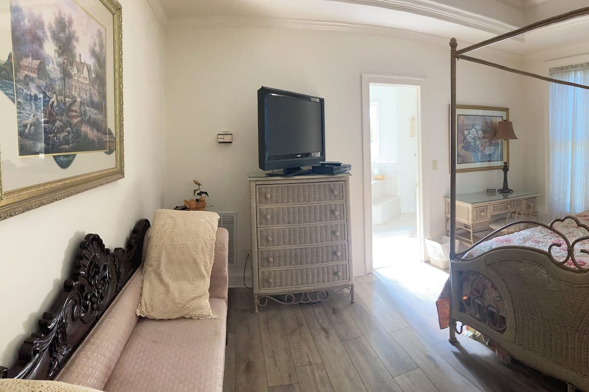A bedroom with a four-poster bed, a dresser, a television, and a painting on the wall.