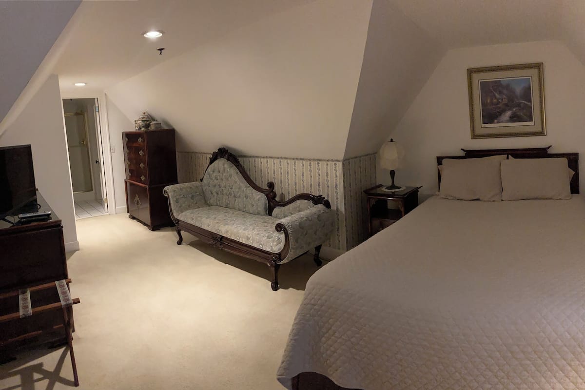 A bedroom with a large bed, a wooden chair, a dresser, and a painting on the wall.