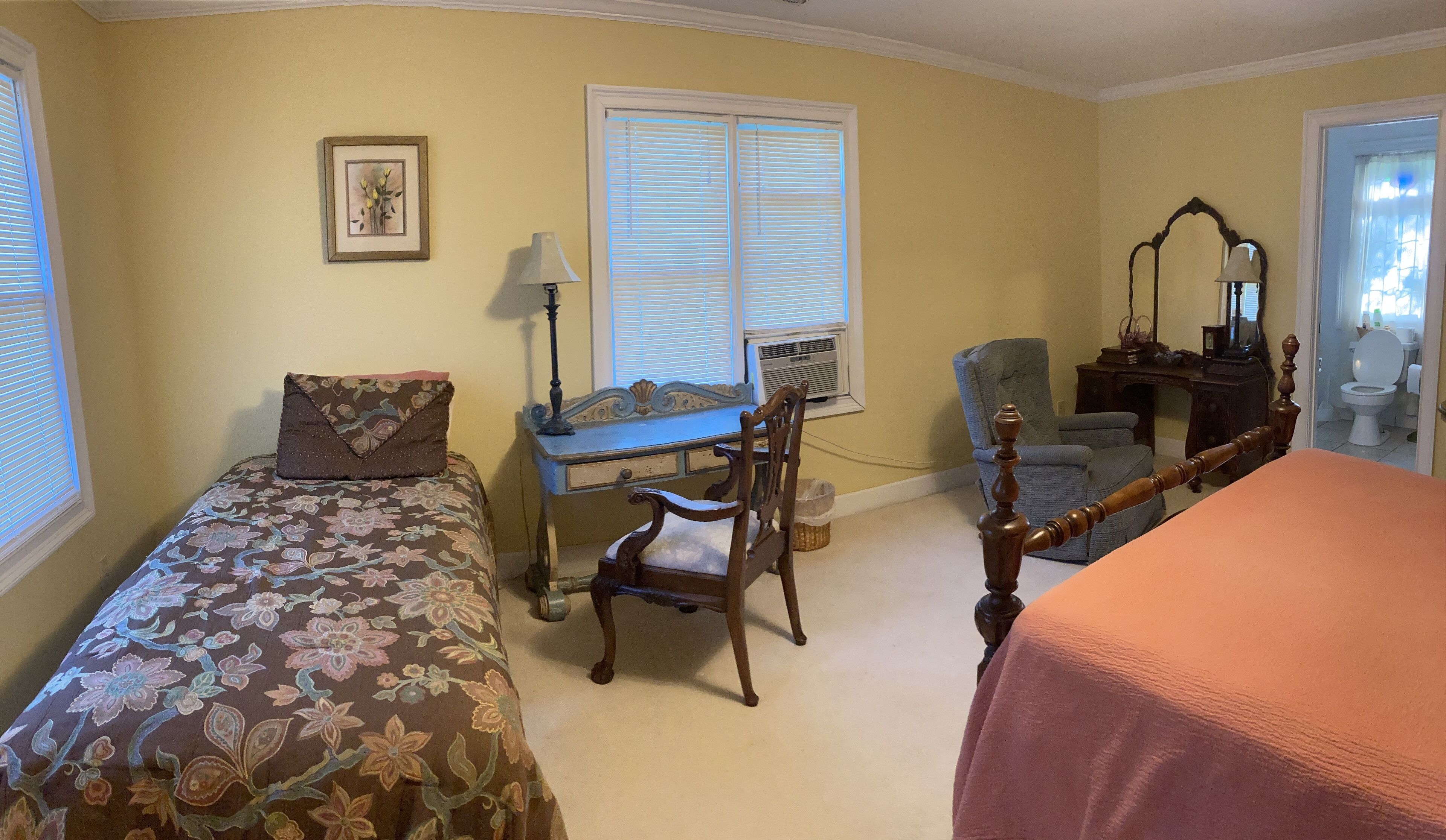 A bedroom with two single beds, a desk, a chair, a dresser, and a window with blinds.