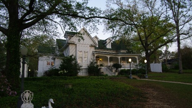 A large, white, two-story house with a porch and a garden in front.
