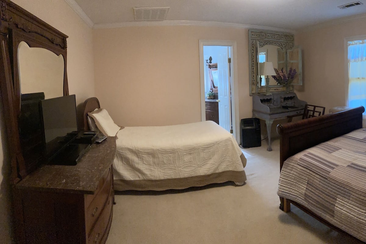 A bedroom with two beds, a dresser, a desk, a mirror, and a window with curtains.