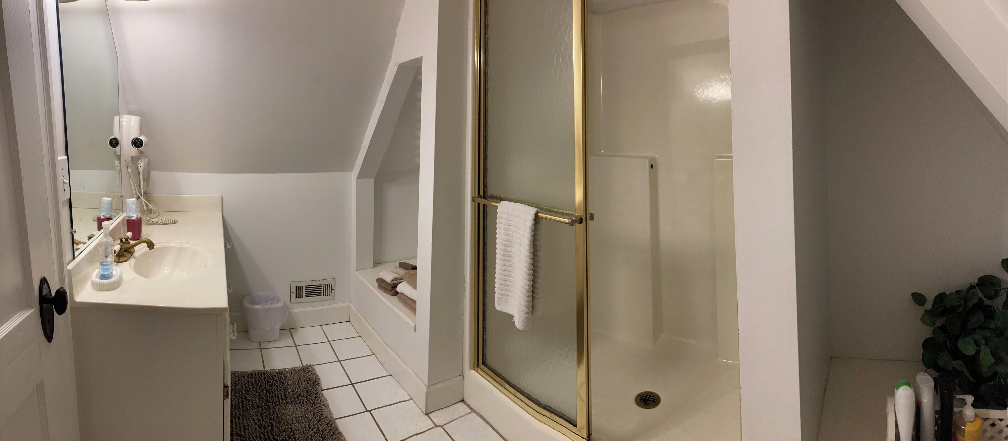 A bathroom with a white sink, a glass shower enclosure, a white towel hanging on the shower door, and a small trash bin.